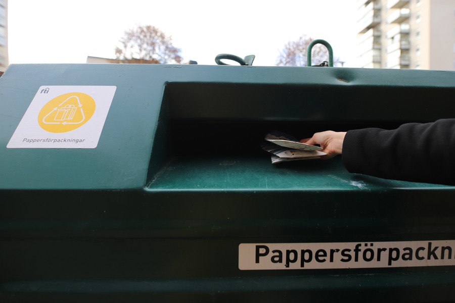 Hand som slänger pappersförpackning på en återvinningsstation