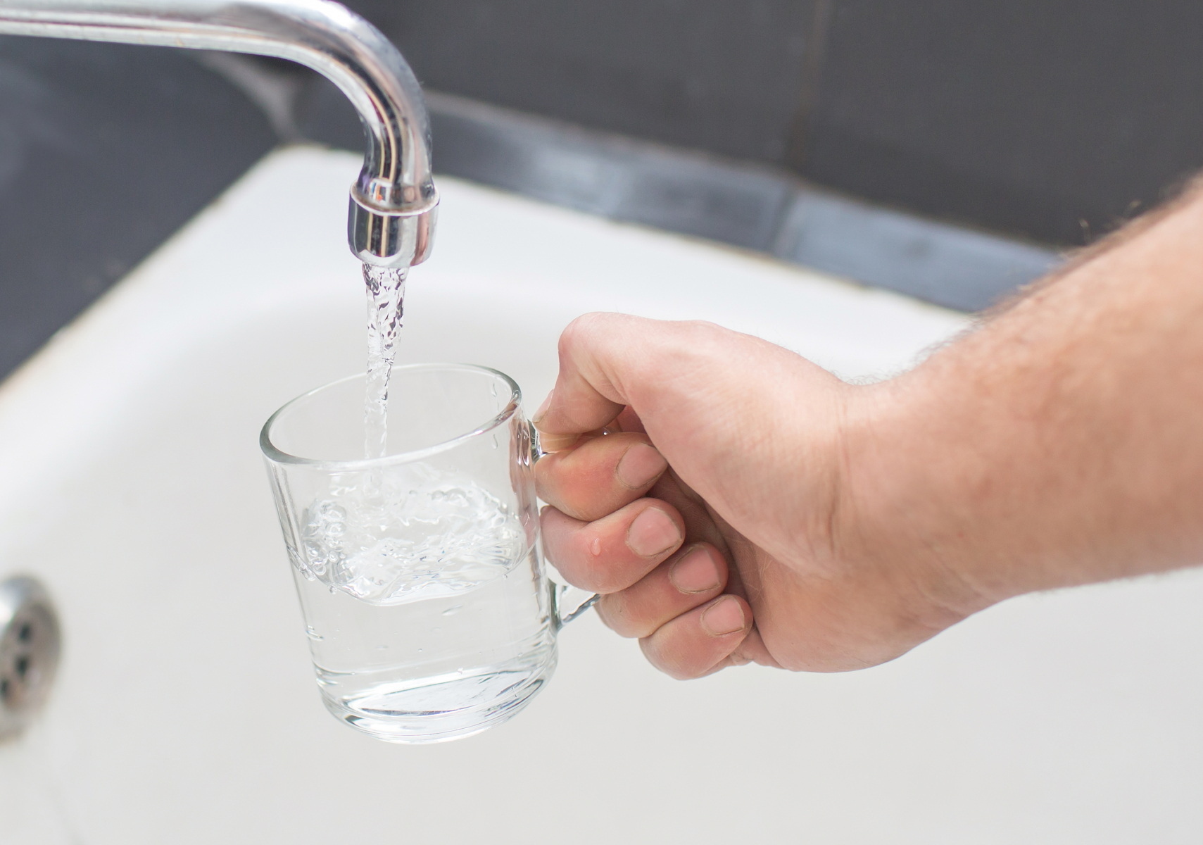Bild på en hand som häller upp ett glas vatten.