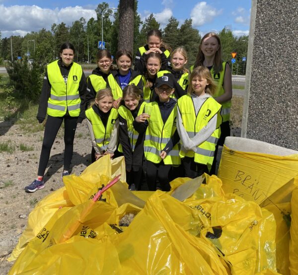 Idrottsungdomar poserar med insamlat skräp i stora gula säckar.